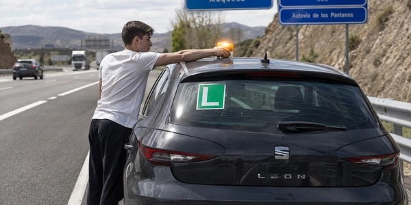Conductor revisando el papel de una multa de tráfico sobre el capó del coche, junto a una señal de circulación prohibida entre la vegetación