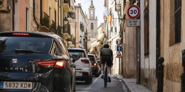 Usuarios vulnerables en un cruce urbano de España: peatón, patinete eléctrico y ciclista con casco ante un coche detenido, según la reforma del Reglamento de Circulación